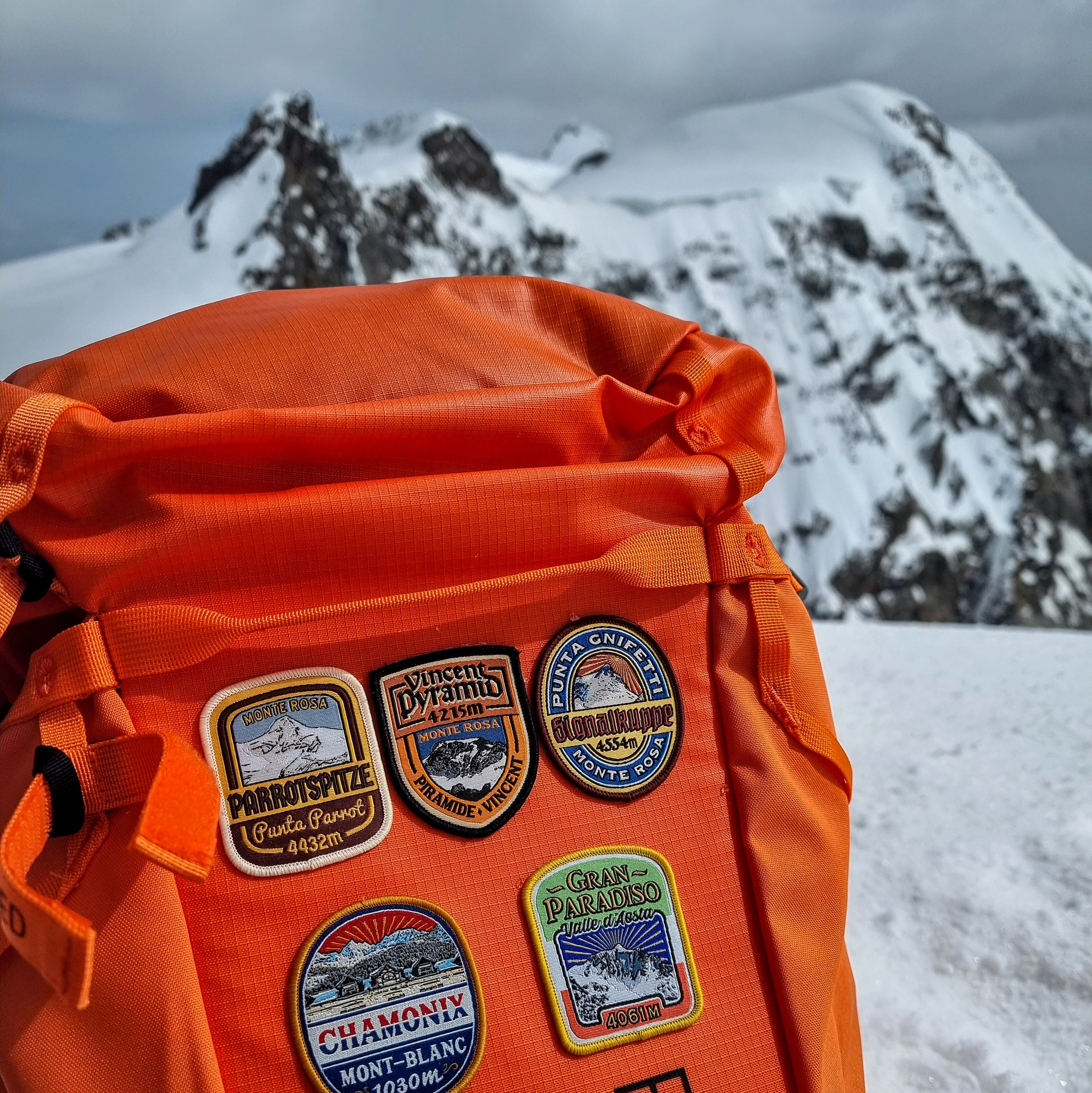 Orange rucksack with Alps patches attached – retro woven Alpine patch collection on outdoor pack